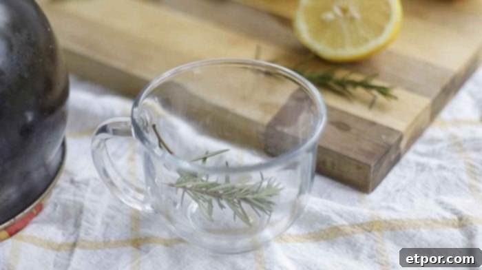 fresh sprigs of rosemary in a glass mug with a cutting board with sliced lemons in the background