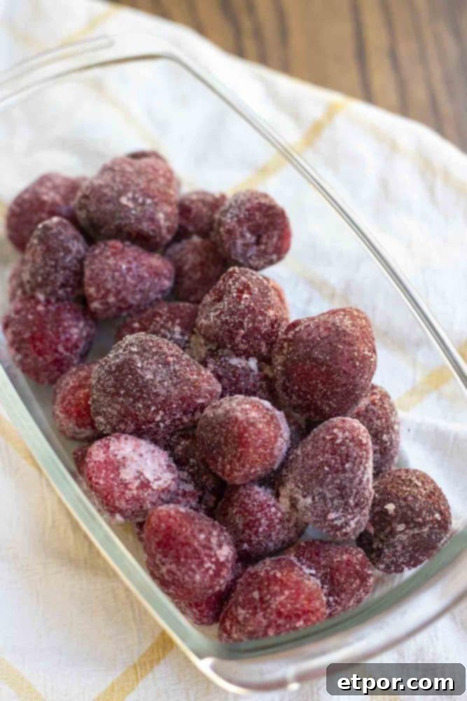 A glass dish filled with vibrant frozen strawberries, resting on a charming white and yellow checked towel.