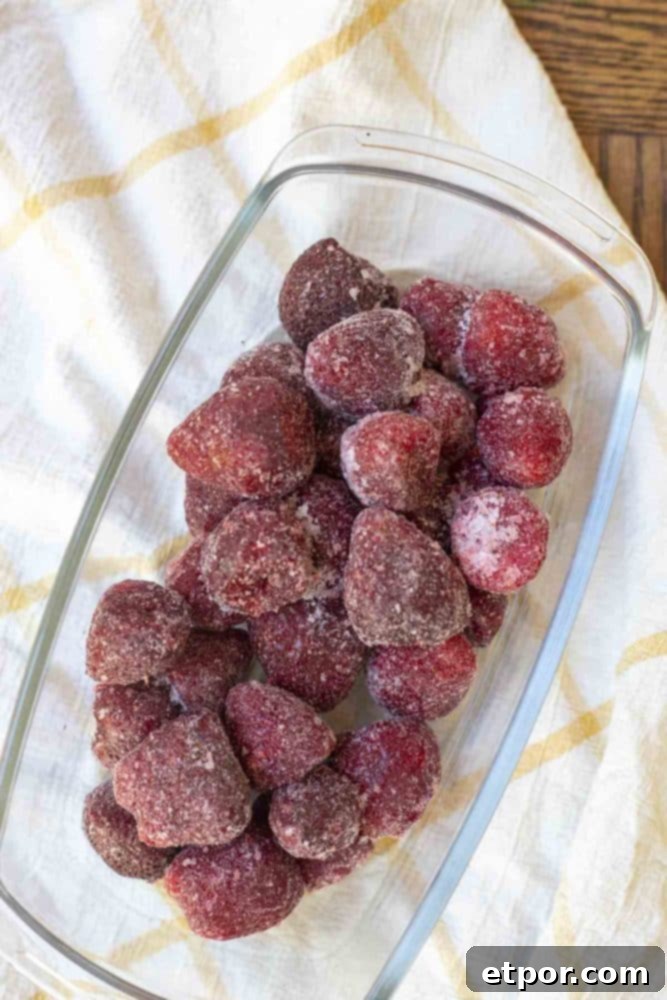 Overhead shot of beautifully frozen strawberries nestled in a glass dish on a rustic white and yellow checked towel.