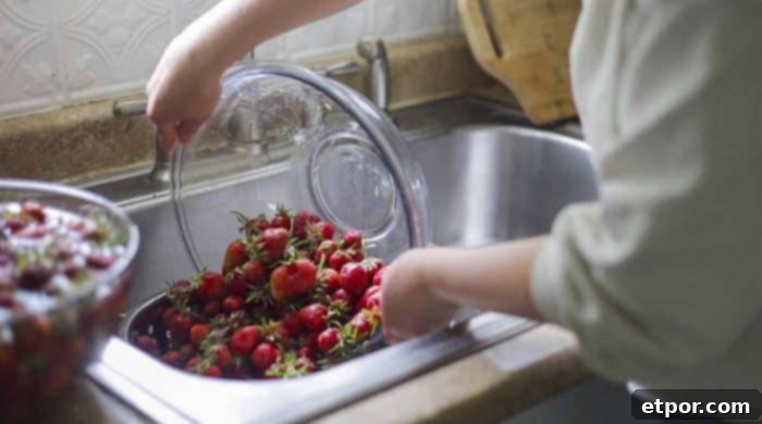 A close-up of a colander filled with freshly washed strawberries, with water still dripping, over a kitchen sink.