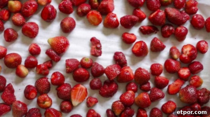 A baking sheet lined with parchment paper, evenly covered with whole and sliced strawberries, prepared for freezing.