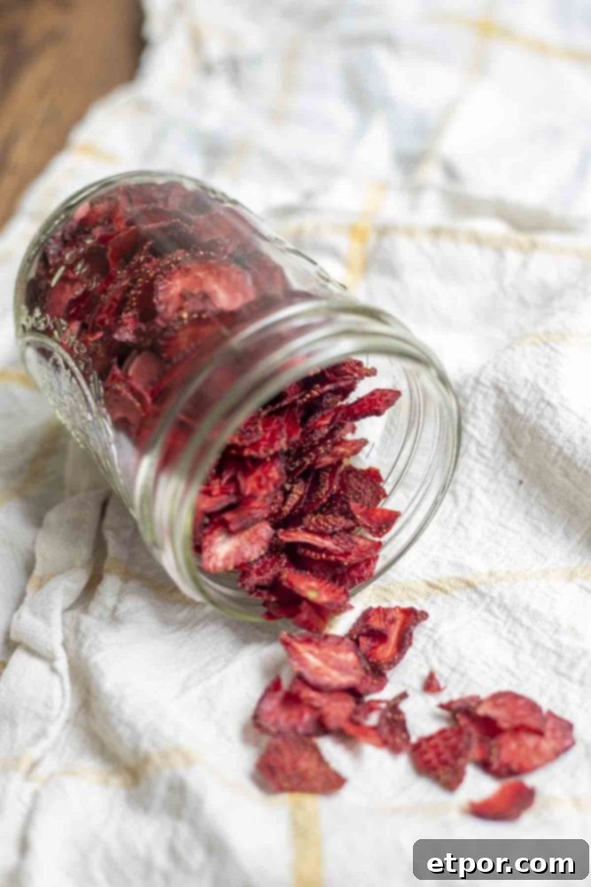 Mastering Homemade Dehydrated Strawberries 4 dehydrated strawberries in a mason jar tipped over and spilling out on a white and yellow checked towel