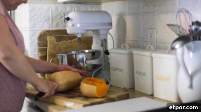 Hands cutting a butternut squash on a cutting board in a clean white kitchen, preparing it for roasting.