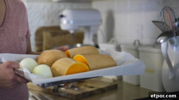 A pair of hands arranging butternut squash halves and onion pieces on a parchment-lined baking sheet, ready for roasting.