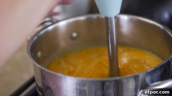 An immersion blender actively blending roasted butternut squash and broth directly in a large pot, creating a smooth, creamy soup texture.