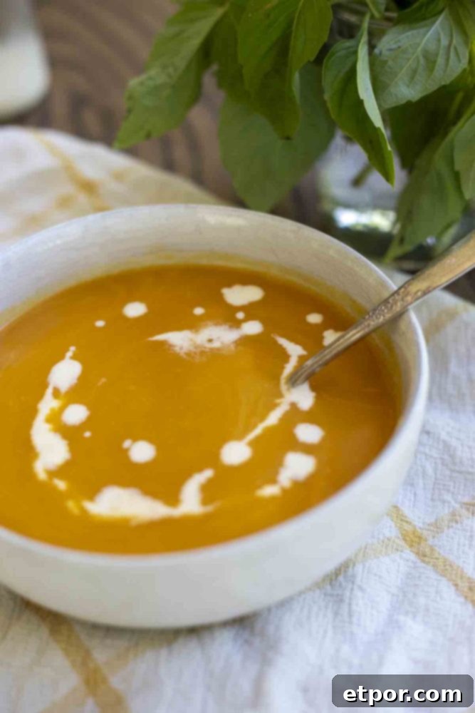 A pristine white bowl of butternut squash soup, elegantly topped with a delicate drizzle of cream. A spoon rests invitingly in the soup, all presented on a cheerful white and yellow checkered towel on a warm wooden countertop, with fresh basil in the background.