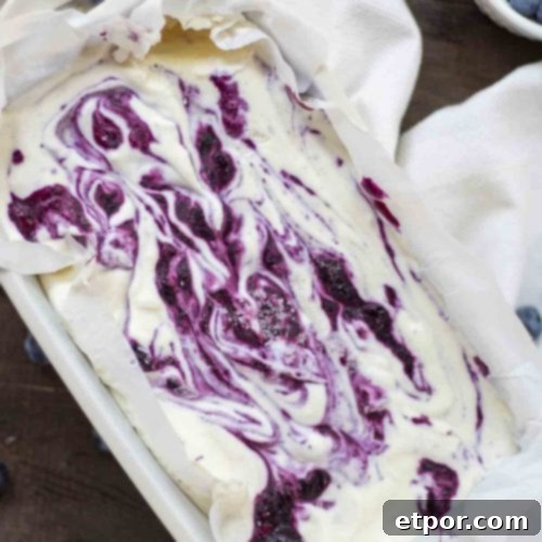 Velvety No-Churn Blueberry Cheesecake Ice Cream 11 Overhead photo of a loaf pan lined with parchment paper, full of creamy blueberry cheesecake ice cream with beautiful swirls of blueberry sauce.