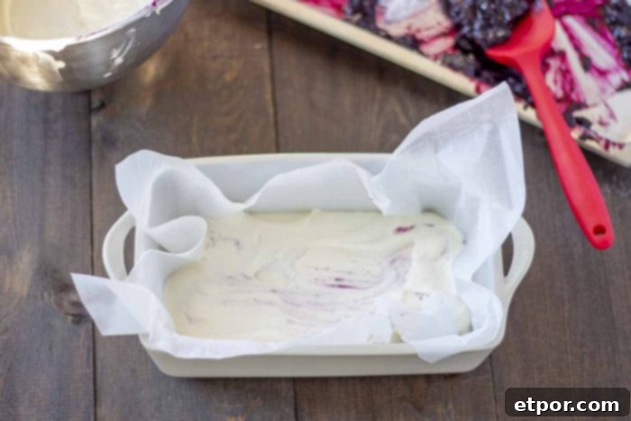 Velvety No-Churn Blueberry Cheesecake Ice Cream 7 Creamy cheesecake ice cream base in a parchment-lined loaf pan, ready for the blueberry swirls. The pan rests on a rustic wooden table.