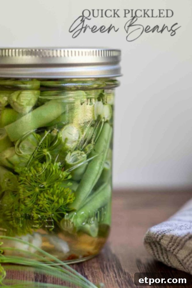 close up picture of quick pickled green beans in a mason jar with fresh dill and garlic. The jar is on a wood table