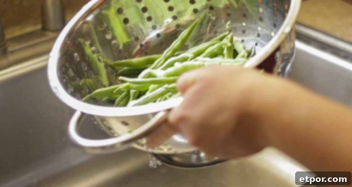 washing green beans in a metal colander in a sink
