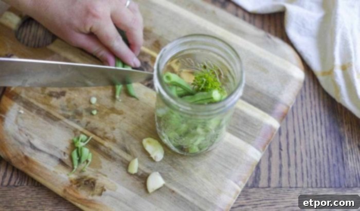 labeling hot brine into a mason jar full of chopped green beans, garlic, and dil on a wood cutting board 