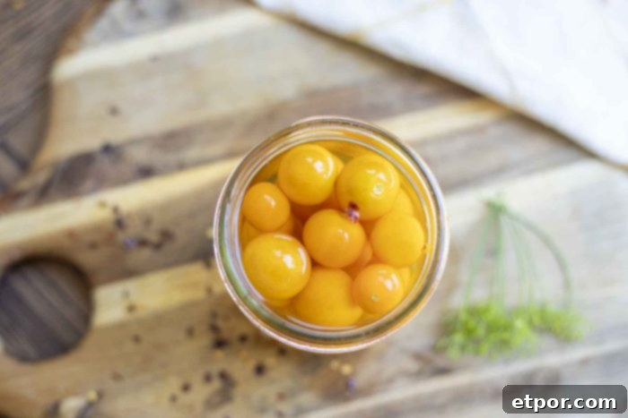 overhead photo of pickled cherry tomatoes in a jar on a wood cutting board
