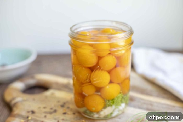 jar of pickled cherry tomatoes with dill and garlic on a wood cutting board with pepper flakes surrounding the jar