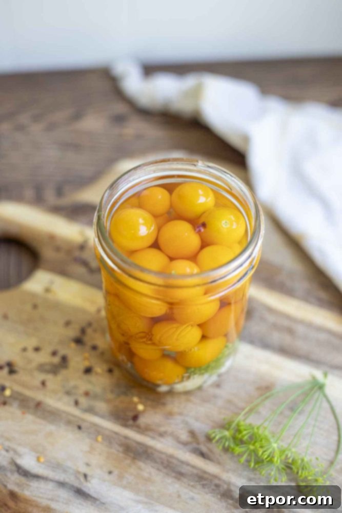 jar of quick pickled cherry tomatoes in a brine on a wood cutting board. 