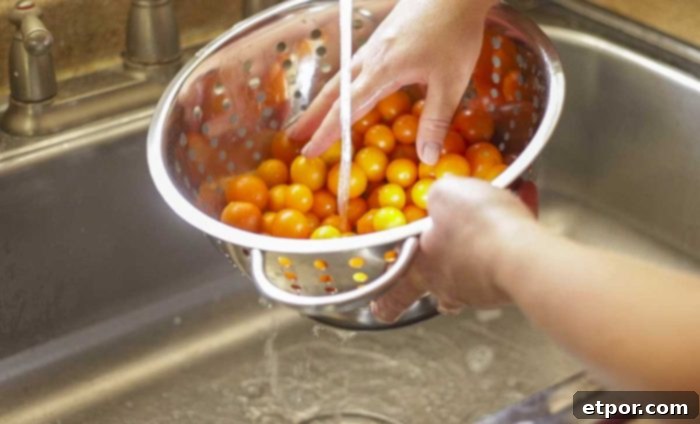cherry tomatoes in a colander being washed in a sink