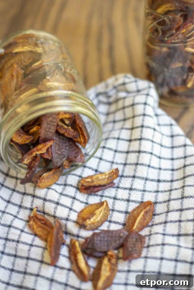 Dehydrated plums spilling out of a mason jar onto a white and black towel on a wood table.