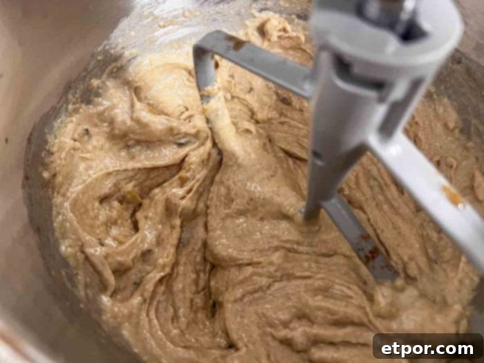 Caramelized apples being carefully added into the sourdough bread batter in a stand mixer bowl with a paddle attachment, ensuring even distribution.