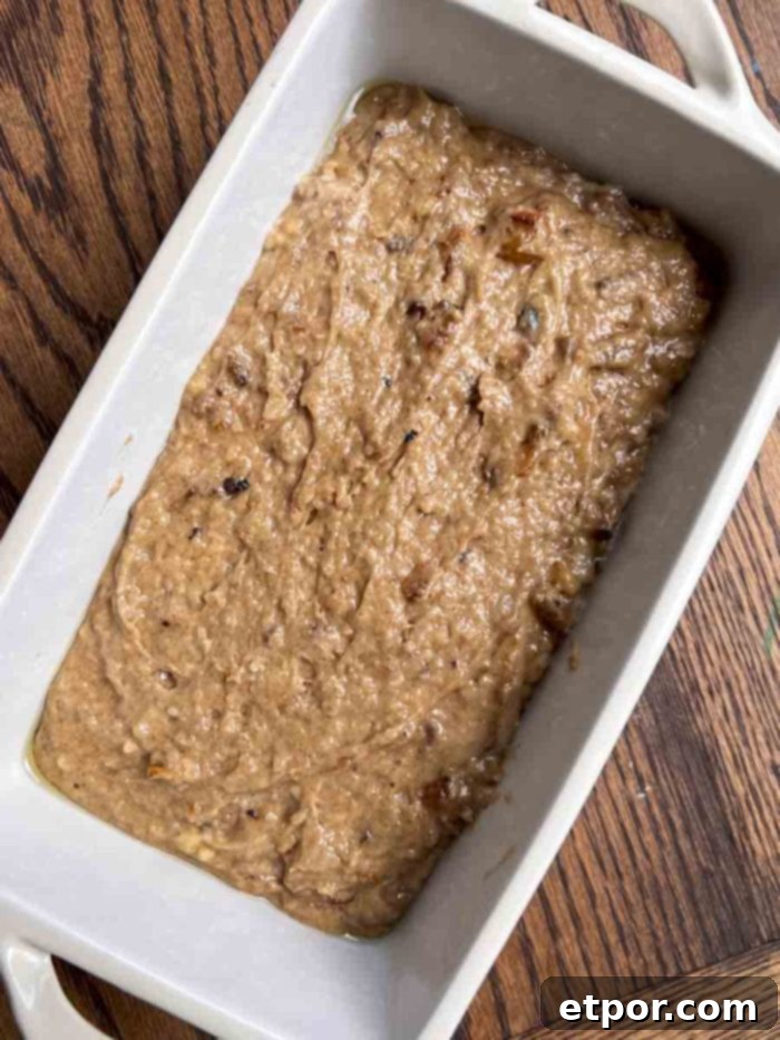 Sourdough apple bread batter ready in a loaf pan on a wooden table, prepared for baking.