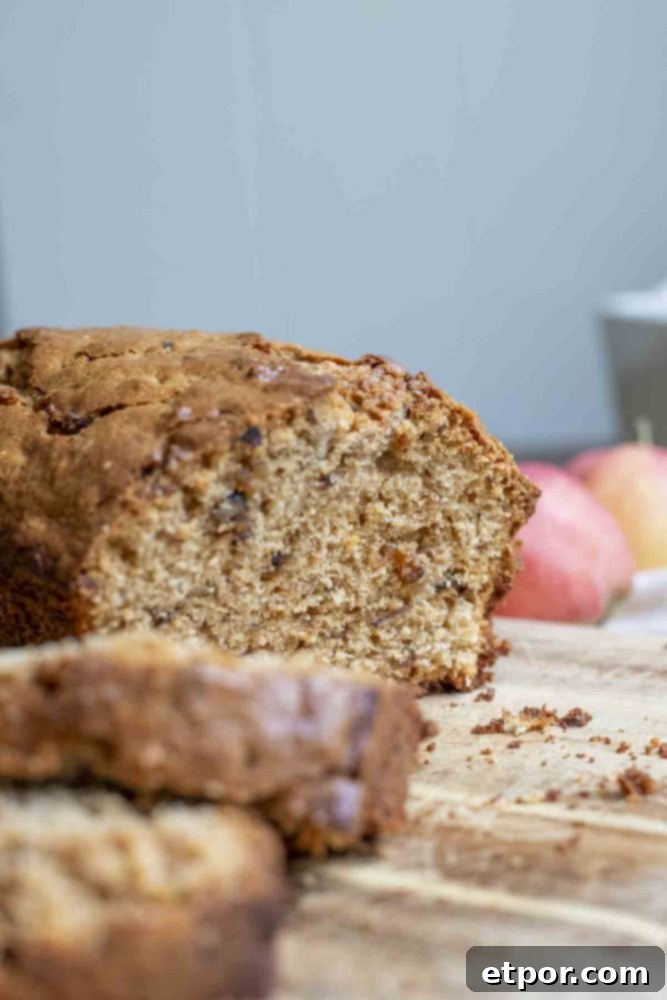 Sourdough apple bread with two slices cut off on a wood cutting board, with fresh apples in the background.