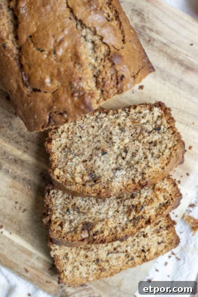 Overhead photo of a loaf of sourdough apple bread with three slices cut off and arranged on a wood cutting board.