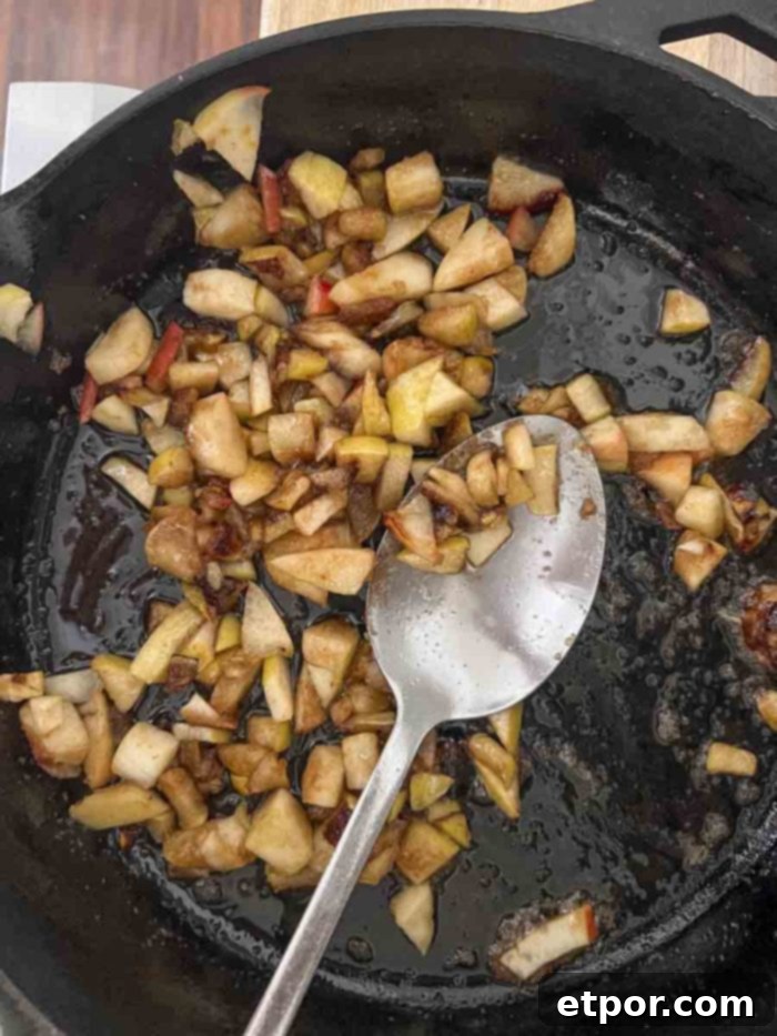 Diced apples in a rich caramel sauce in a cast iron skillet with a metal spoon, ready to be incorporated into the bread batter.