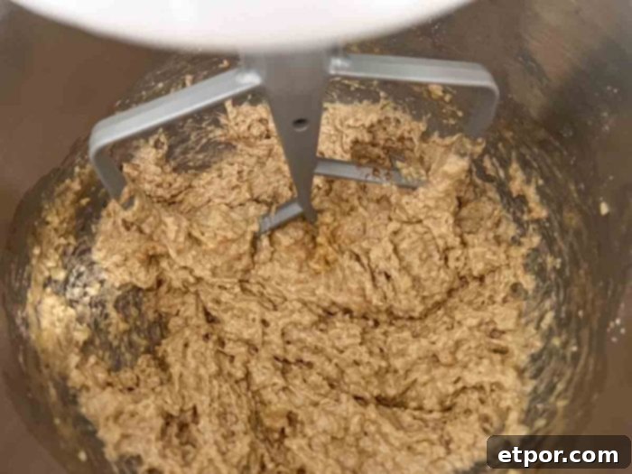 Sourdough apple bread batter actively mixing in a stand mixer with a paddle attachment, achieving a smooth consistency.