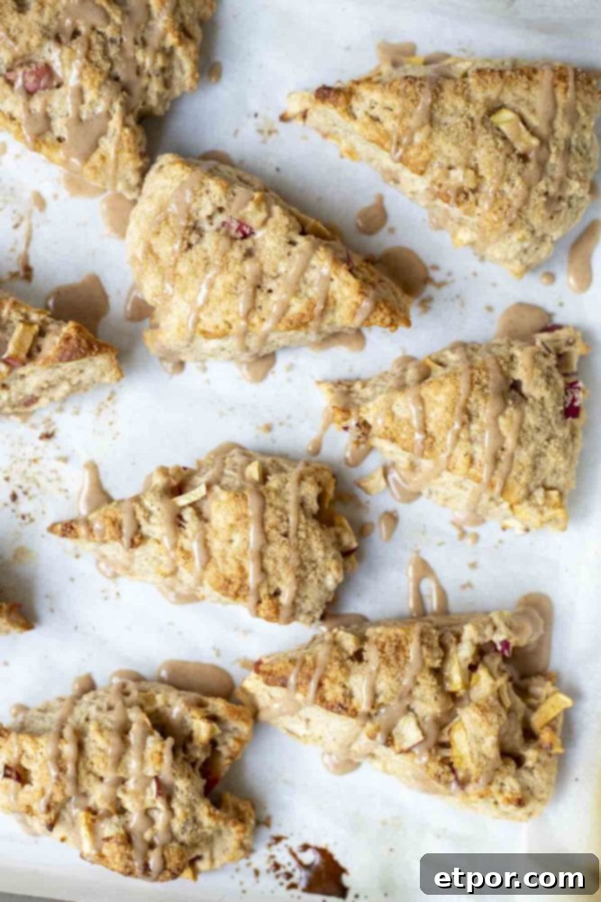 An overhead view of eight perfectly baked sourdough apple scones, generously drizzled with cinnamon glaze, arranged on a parchment-lined baking sheet.