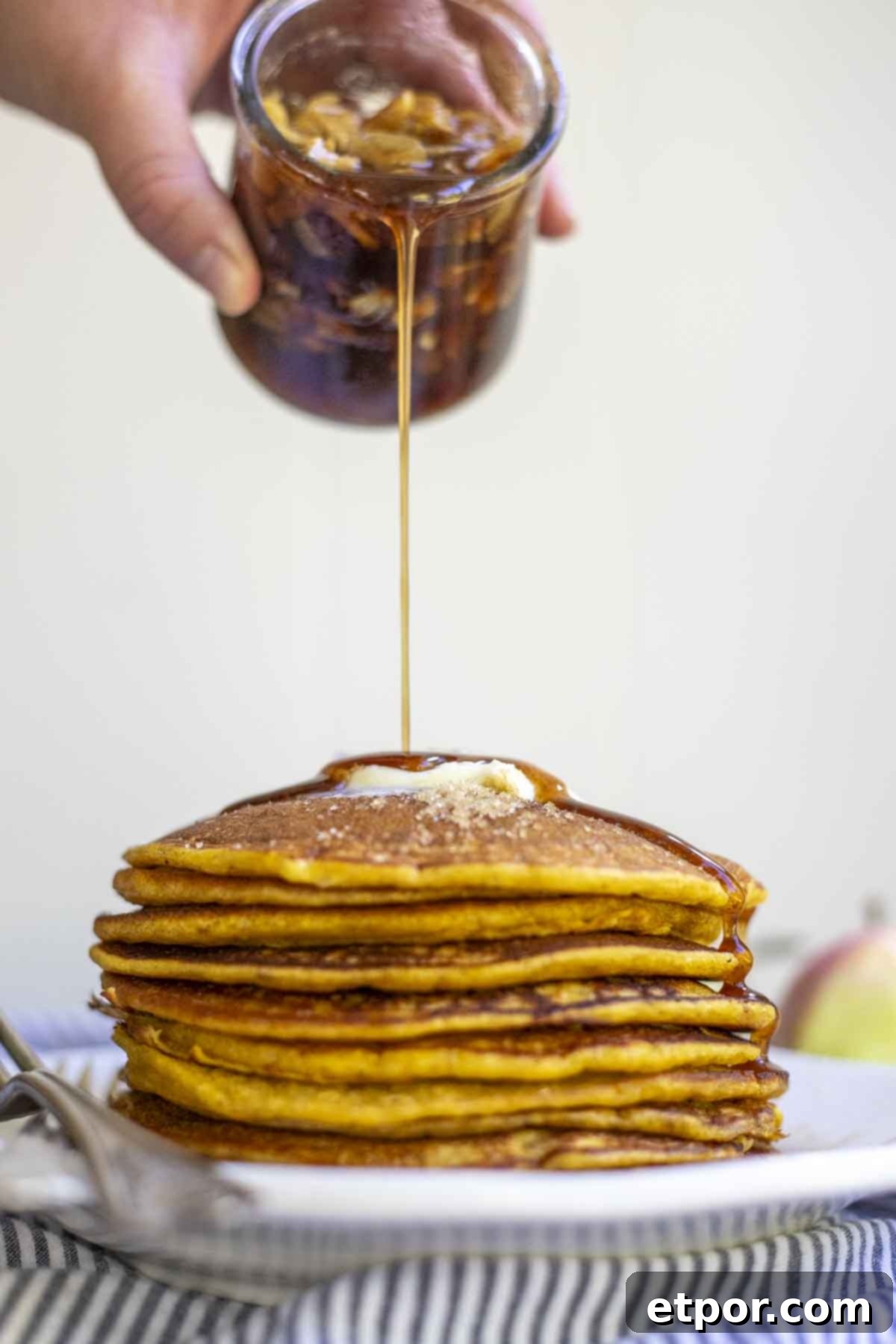 pouring syrup onto a stack of sourdough pumpkin pancakes topped with butter.