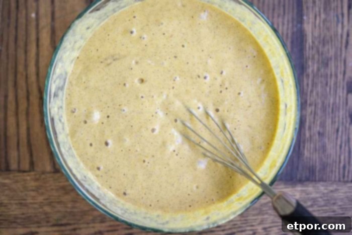 pumpkin sourdough pancake batter in a glass bowl on a wood counter.