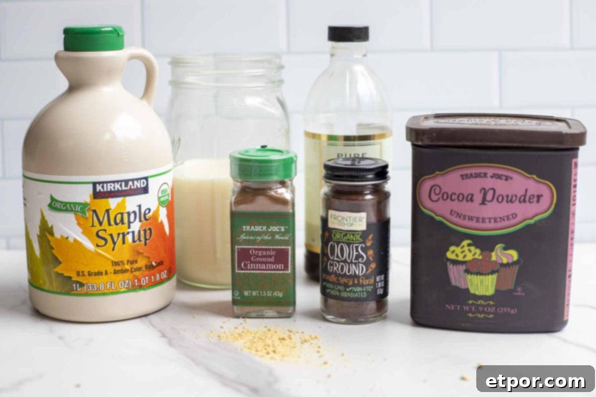 cocoa powder, bottles of spices, vanilla extract, jar of milk, and a bottle of maple syrup on a white countertop.