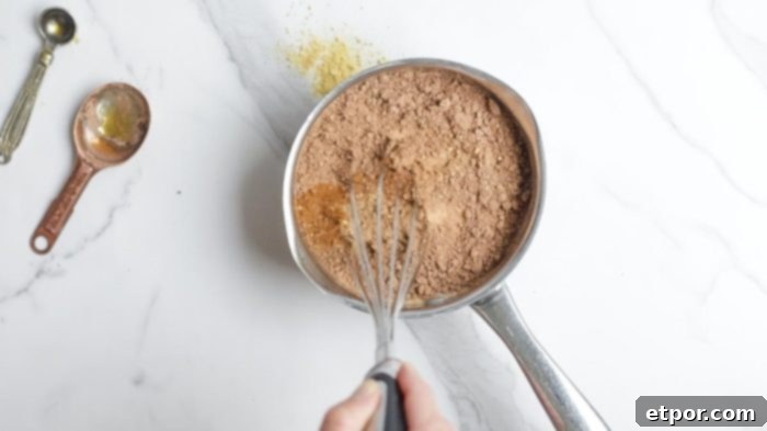 whisking hot chocolate ingredients together in a small saucepan on a white countertop.