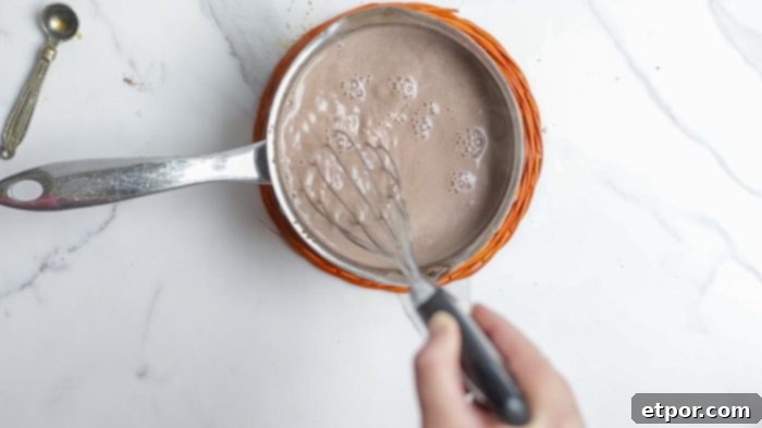 whisking hot cocoa together in a small saucepan on a orange pot holder.