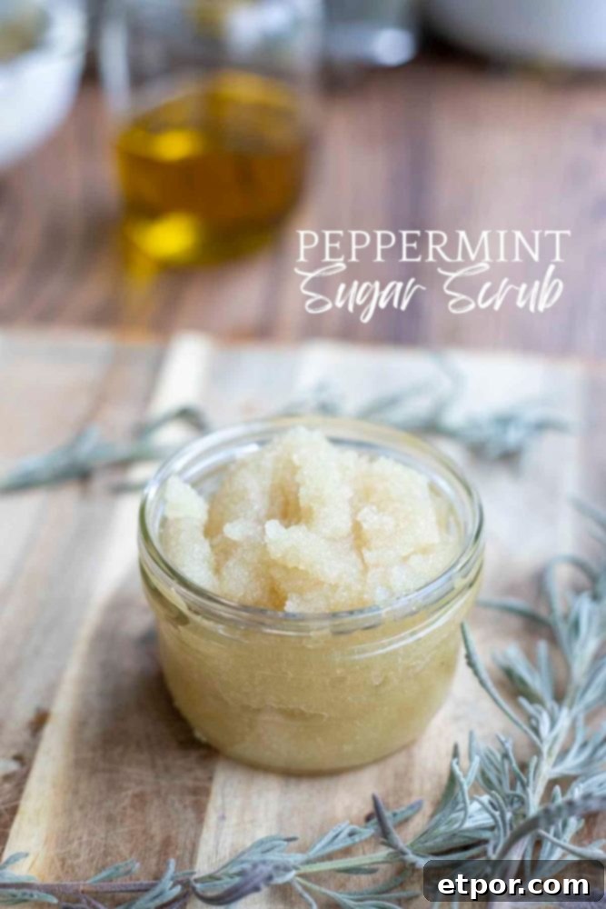 Homemade peppermint sugar scrub in a glass mason jar on a wood cutting board surrounded by lavender. A jar of oil is in the background