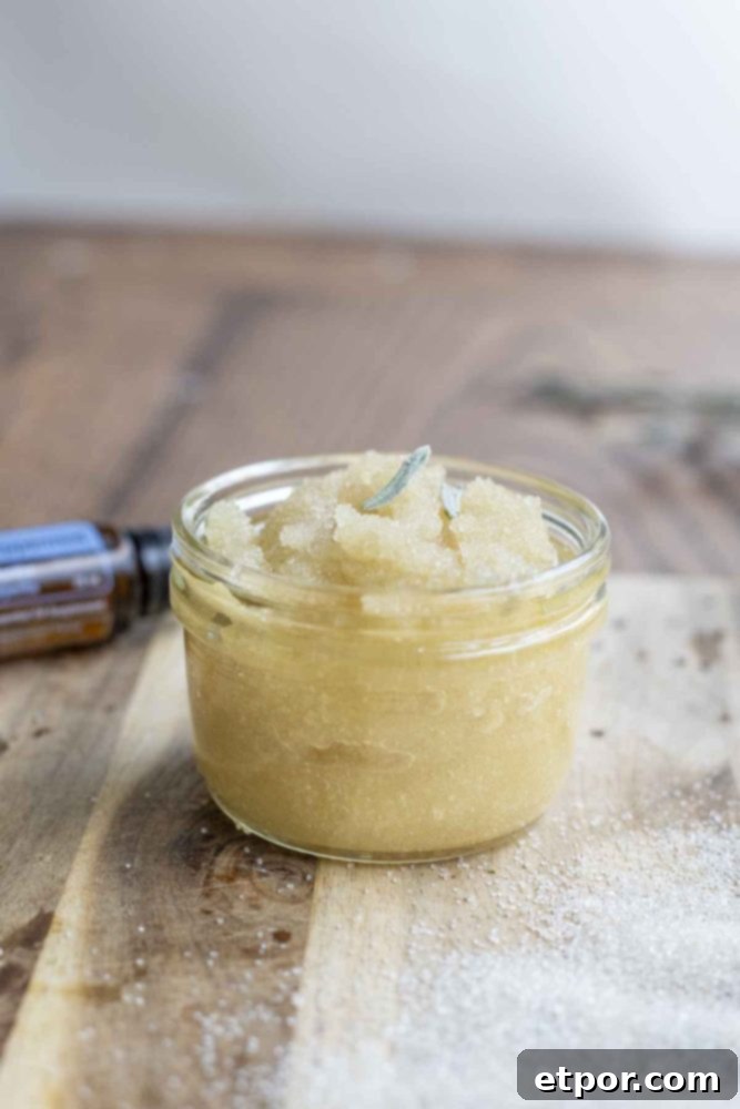 peppermint sugar scrub in a small mason jar on a wood countertop with a bottle of peppermint essential oil in the background
