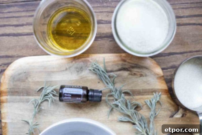 Jars of sugar, oil, and bottle of peppermint essential oil on a wood cutting board with fresh lavender 