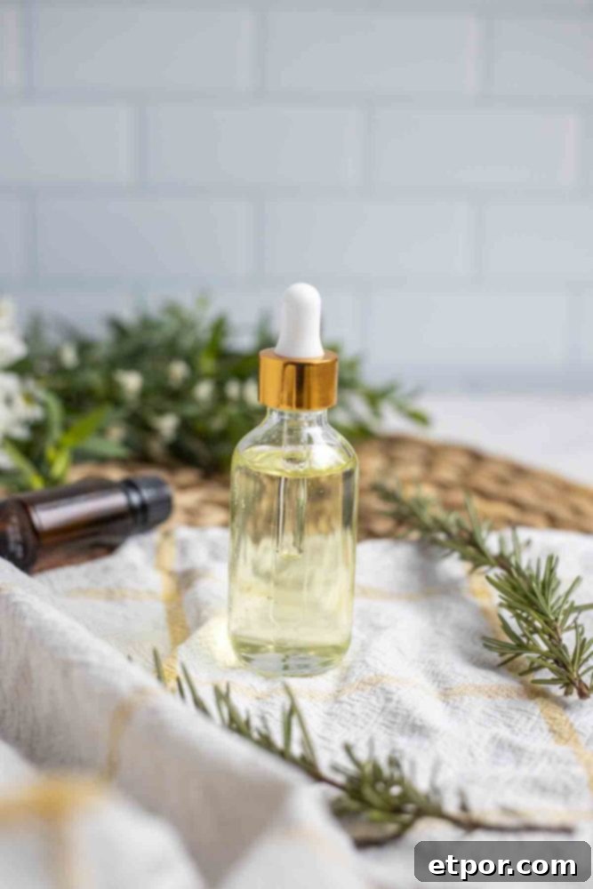 Boost Hair Growth with Homemade Rosemary Oil 12 Glass bottle with dropper of rosemary hair growth oil on a white and yellow napkin with fresh sprigs of rosemary surrounding the jar. There is a small bouquet of greenery in the background