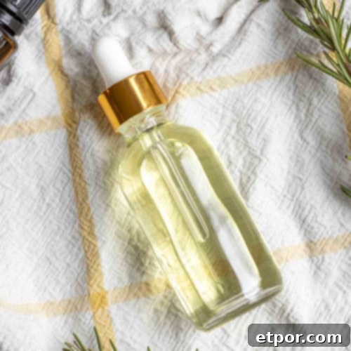 Boost Hair Growth with Homemade Rosemary Oil 13 overhead photo of a bottle of rosemary hair oil laying on a white and yellow plaid towel surrounded by rosemary