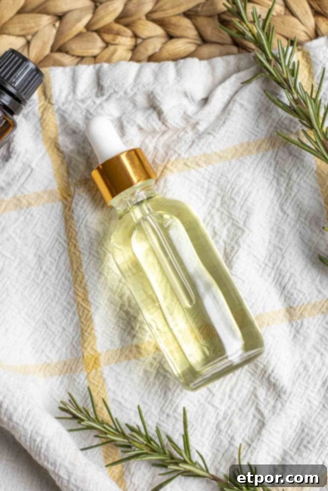 Boost Hair Growth with Homemade Rosemary Oil 3 overhead photo of a bottle of rosemary hair oil laying on a white and yellow plaid towel surrounded by rosemary