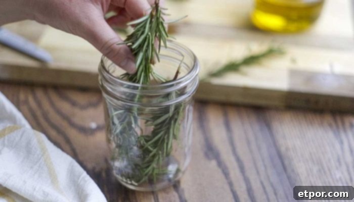 Boost Hair Growth with Homemade Rosemary Oil 8 adding rosemary sprigs to a jar with a cutting board in the background