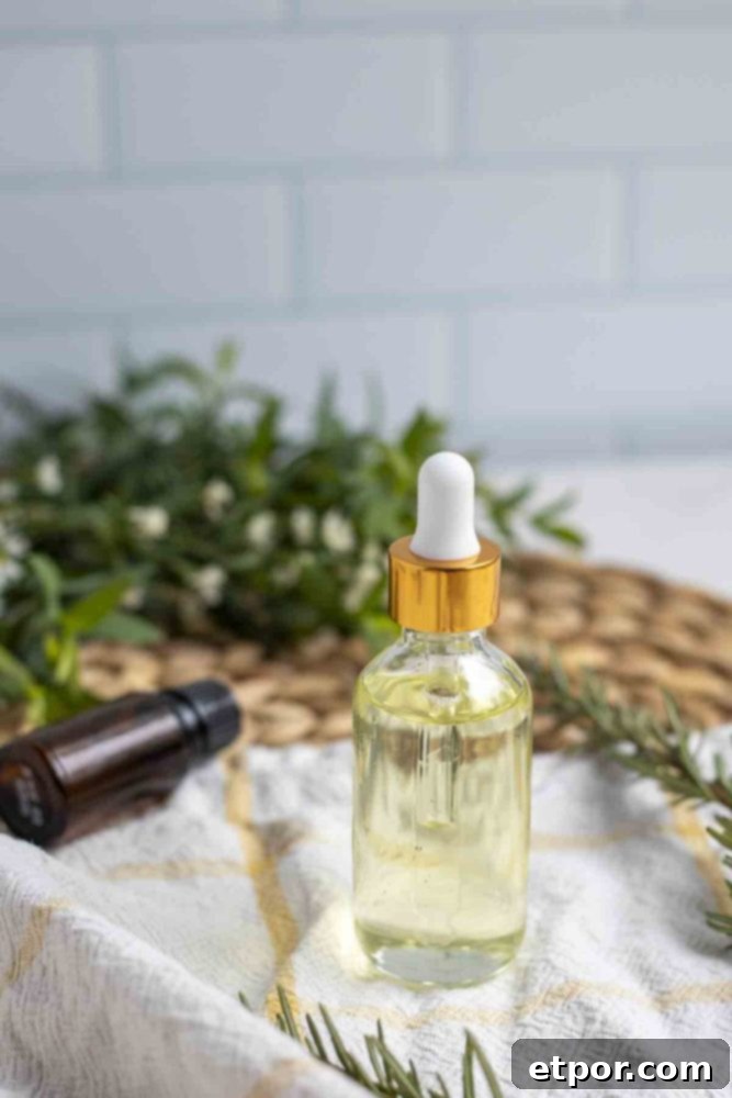 Boost Hair Growth with Homemade Rosemary Oil 10 a glass dropper bottle of rosemary oil on a white and yellow towel with fresh greenery and an essential oil bottle in the background