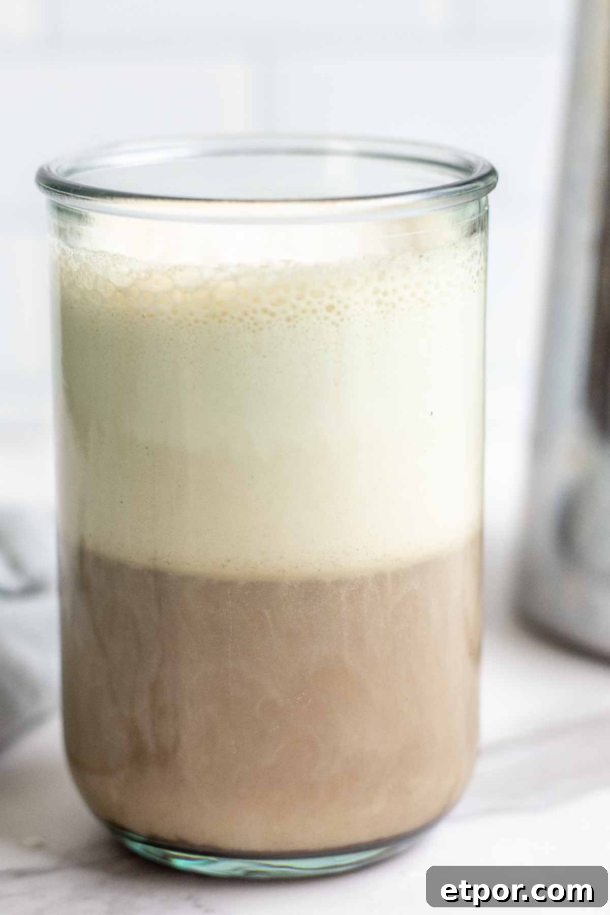 close up photo of coffee topped with cold foam in a glass with a French press in the background.