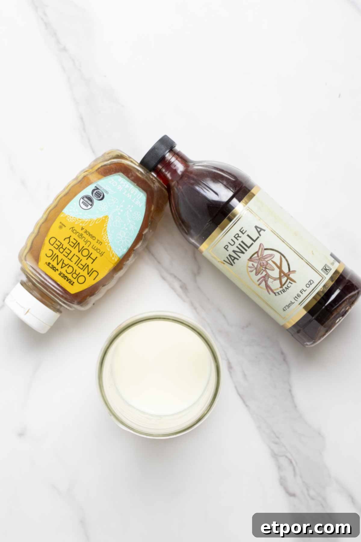 a bottle of honey, a bottle of vanilla extra, and a jar of milk on a marble counter.