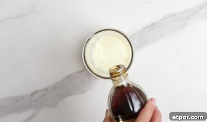 vanilla extract being added to a jar with milk on a marble countertop.