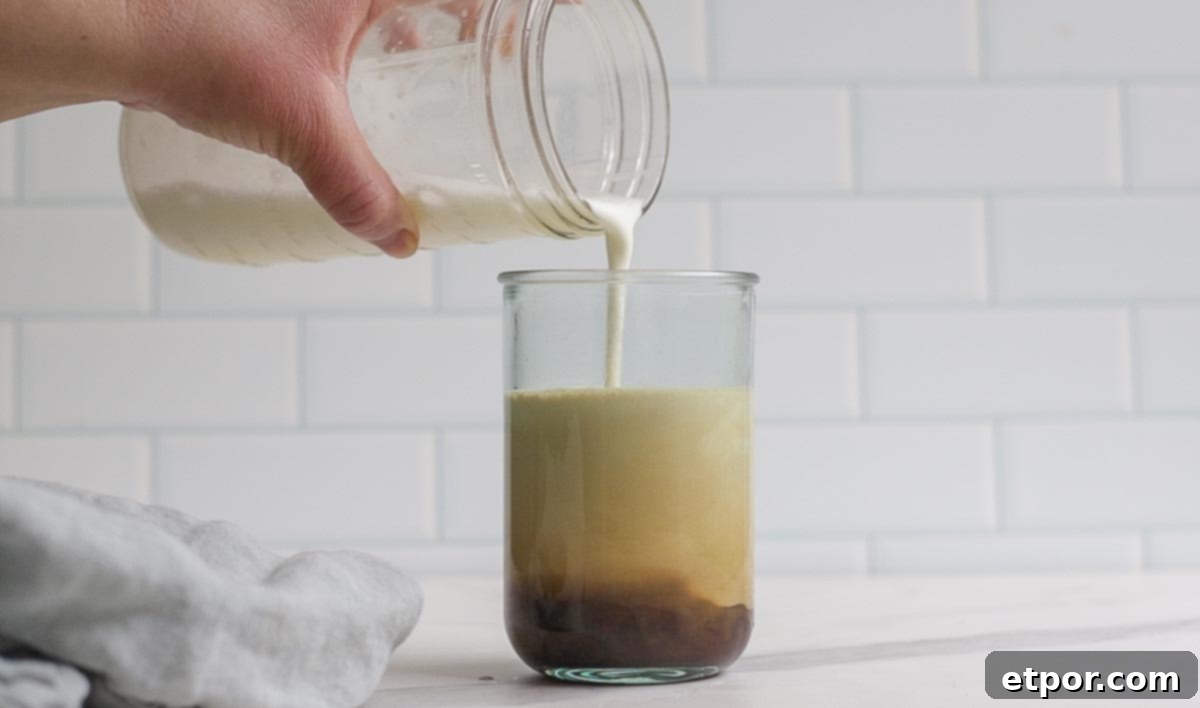 pouring cold foam on top of coffee in a glass.