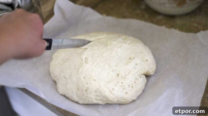 slicing sourdough discard bread dough with a knife on parchment paper