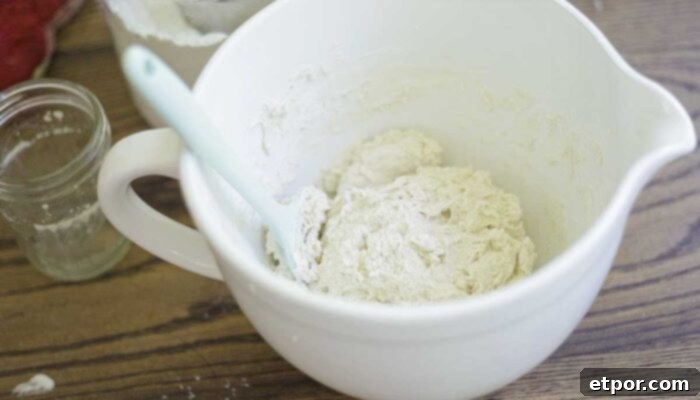 bread dough in a white stand mixer bowl with teal spatula