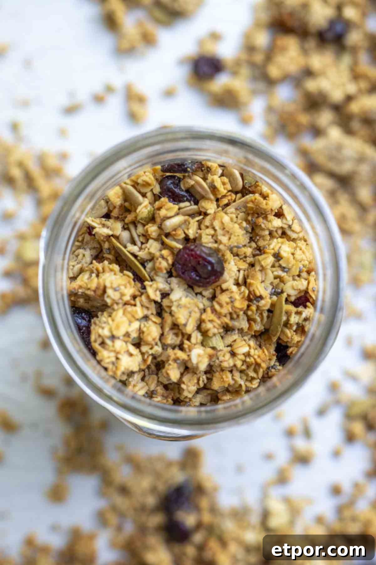Overhead photo of sourdough granola with seeds and dried cranberries in a mason jar. The jar is on a parchment lined baking sheet with more granola.