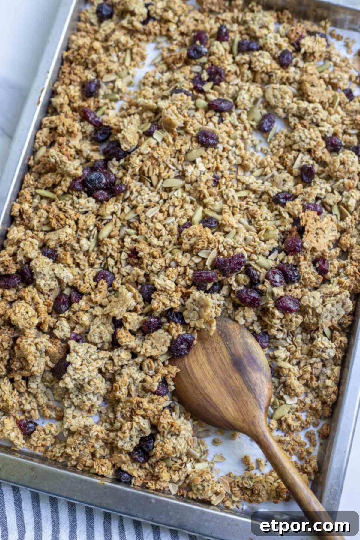 Sourdough granola with sunflower seeds, pumpkin seeds, and dried cranberries on a parchment lined baking sheet with a wooden spoon.