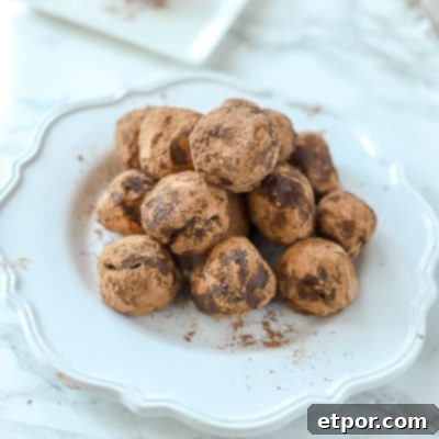 A close-up shot of perfectly stacked vegan chocolate truffles on a white scalloped plate, set against a sleek marble countertop, highlighting their rich, dark allure and inviting texture.