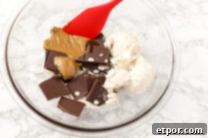 5 Malzemeli Baştan Çıkarıcı Vegan Trüf 7 A glass bowl positioned over a simmering pot of water, forming a double boiler setup. Inside the bowl, the ingredients for vegan truffles—dark chocolate, coconut cream, and nut butter—are visibly melting and combining into a smooth, glossy ganache.